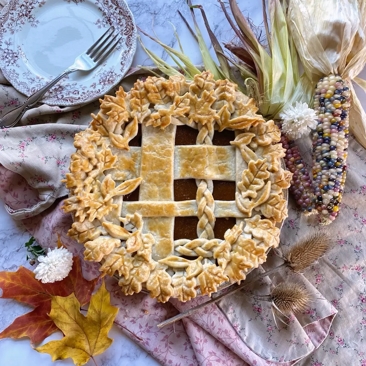Fall harvest pie with hand-cut pastry leaves, autumn decor, and dried corn