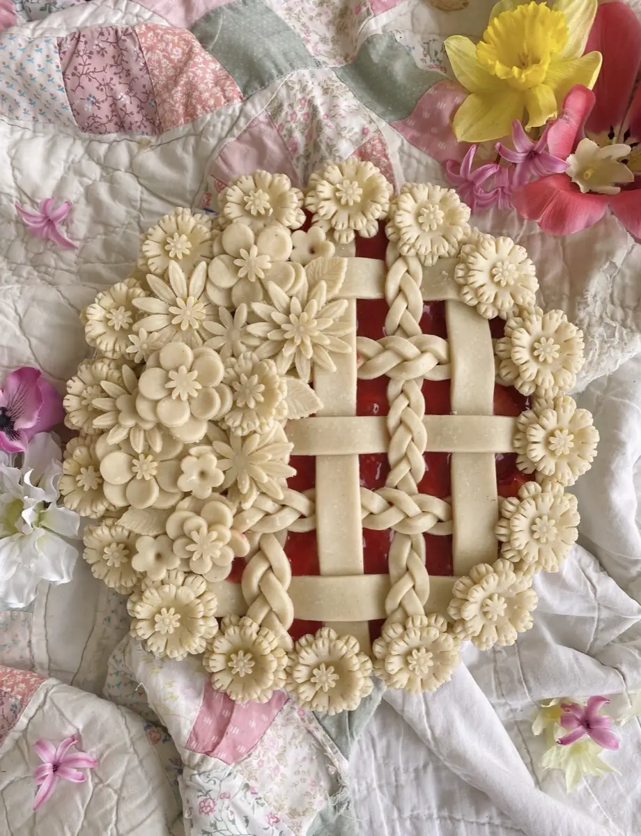 Intricate floral lattice pie with hand-cut pastry flowers on a vintage quilt