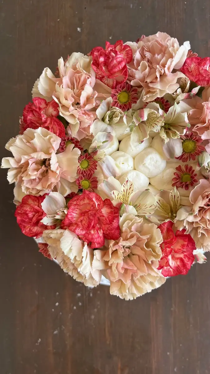Overhead view of a cake covered in pink and cream carnations